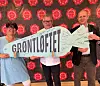 Tre personer står foran en rød vegg og holder en stor plakat med teksten «GRØNTLØFTET».