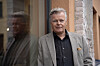 En mann i grå blazer står ved en inngang med murvegg og vindu.