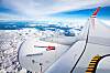 Utsikt fra et Norwegian-fly over snødekte fjell og skyer, med vingen og motoren i forgrunnen.