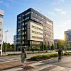 Moderne kontorbygg med glassfasade ved en gate, med en fotgjenger og en syklist i forgrunnen.