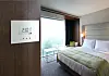 Moderne hotellrom med seng, kontrollpanel på veggen og stor åpning mot balkong og utsikt.