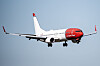 Norwegian-passasjerfly med rødt neseparti på himmelen under innflyging.