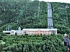 Stort industribygg i grønn skogkledd dal med kraftlinjer og høyt tårn.