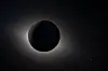 Mørk måneskive foran solen med en svak lysglorie i verdensrommet.