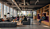Moderne kontorlounge med mennesker, arbeidsplasser, planter og store vinduer.