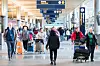 Reisende med bagasje i en travel flyplassterminal med informasjonsskilt.