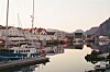 Fiskebåter i en stille havn med hvite hus og fjell i bakgrunnen.