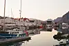 Fiskebåter i en stille havn med hvite hus og fjell i bakgrunnen.