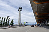 Flyplasstårnet ved Oslo lufthavn Gardermoen, med terminalinngang, biler og reisende i forgrunnen.