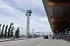 Flyplasstårnet ved Oslo lufthavn Gardermoen, med terminalinngang, biler og reisende i forgrunnen.