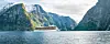 Hvitt cruiseskip på fjord omgitt av bratte, grønne fjell.