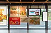Restaurantplakater med matbilder og tilbud vist i store vinduer.