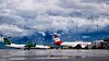 Passasjerfly på en våt flyplassrampe under mørke skyer, med et Air India-fly i sentrum.