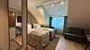 Moderne hotellrom med oppredd seng, sofa, lenestol og store vinduer.