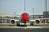 Norwegian-fly sett forfra på en flyplass, med rødt neseparti og to motorer.
