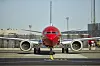 Norwegian-fly sett forfra på en flyplass, med rødt neseparti og to motorer.