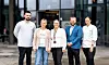 Fem kolleger poserer foran et moderne kontorbygg.