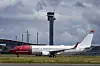 Norwegian-fly på bakken ved Gardermoen med flytårnet og skyer i bakgrunnen.