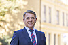 Dresskledd mann foran en lys bygning og grønne trær.