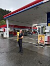 Person foran en YX-bensinstasjon med drivstoffpumper på våt asfalt.