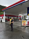 Person foran en YX-bensinstasjon med drivstoffpumper på våt asfalt.