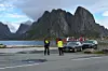 To personer i refleksklær ved stansede biler foran bratte fjell og sjø.
