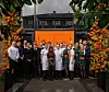 Gruppe mennesker poserer foran en bygning med oransje dør og blomstrende planter.
