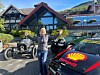 Kvinne mellom veteranbiler og en Shell-merket sportsbil foran et fjellhotell.