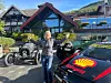Kvinne mellom veteranbiler og en Shell-merket sportsbil foran et fjellhotell.