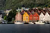 Fargerike trehus ved vannet med båter og skogkledde fjell i bakgrunnen.