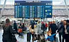 Reisende med bagasje i innsjekkingshallen på Oslo lufthavn, under en stor digital avgangstavle.