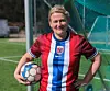 Fotballspiller i norsk drakt holder en ball foran et mål på en kunstgressbane.