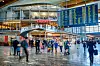 Reisende i den lyse avgangshallen på Oslo lufthavn Gardermoen under store flyinformasjonstavler.