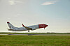 Norwegian-fly flyr lavt over en rullebane med grønt gress og blå himmel.