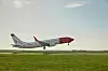 Norwegian-fly flyr lavt over en rullebane med grønt gress og blå himmel.