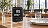 QR-plakat for bestilling står på et kafébord med glass og servise.