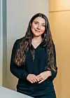 Smilende kvinne med langt mørkt hår står foran en lys vegg og trepanel.