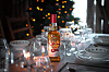 Festbord med glass, servise og en flaske med ravfarget drikke foran et juletre.