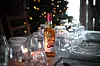 Festbord med glass, servise og en flaske med ravfarget drikke foran et juletre.
