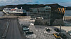 Cruiseskip ved en moderne havnefront med glassbygning, veier og biler.