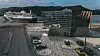 Cruiseskip ved en moderne havnefront med glassbygning, veier og biler.